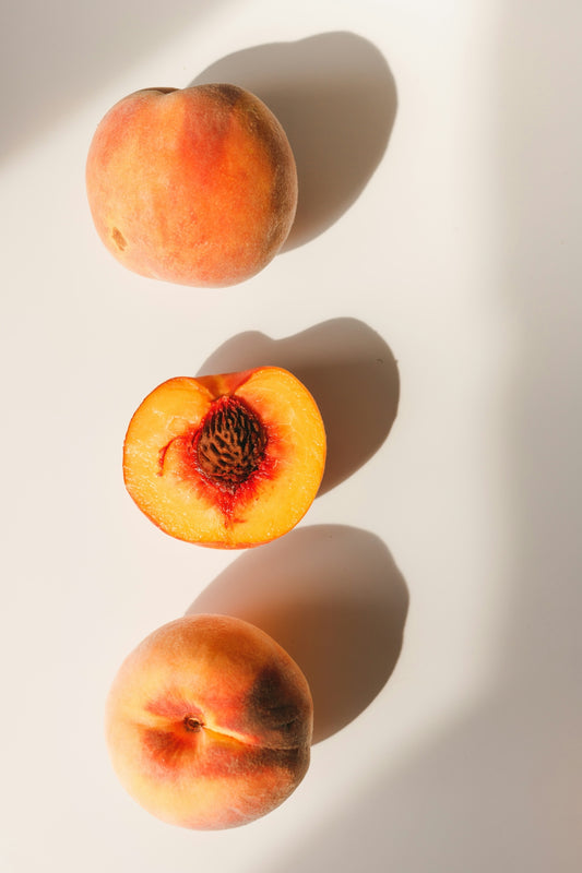 Two whole peaches and one halved peach with a pit on a white surface