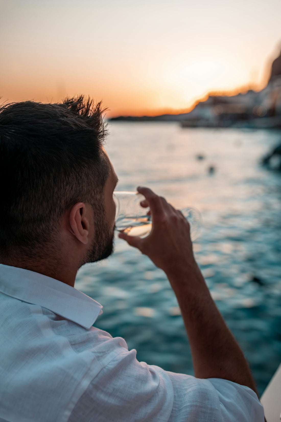 Man sips drink, watching fira sunset
